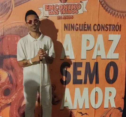 Felipe de óculos e segurando uma bengala em frente a painel onde se lê "ninguém constrói a paz sem o amor"