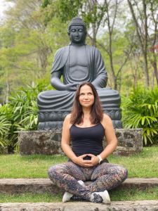 Sandra Teschner sentada com pernas cruzadas em frente a uma estátua de Buda