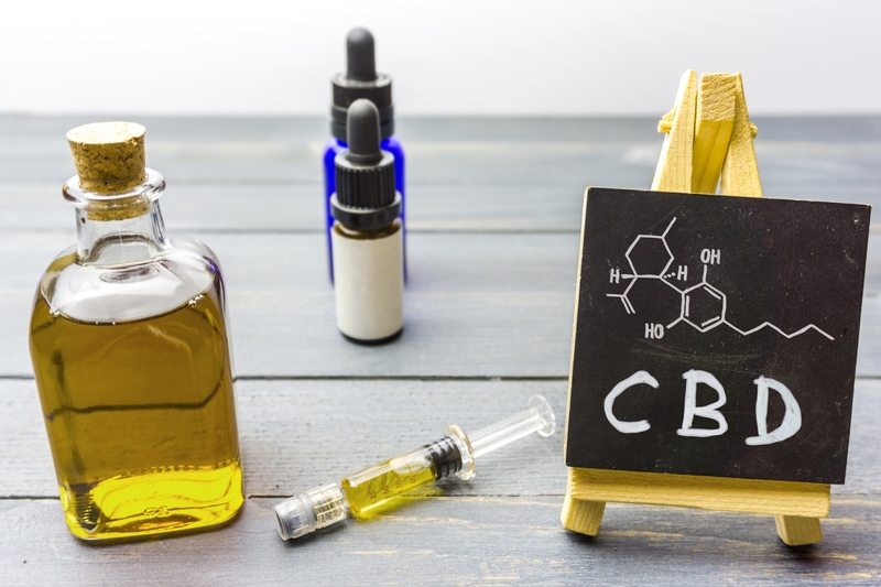Molécula de CBD escrita em quadro ao lado de frascos contendo óleos