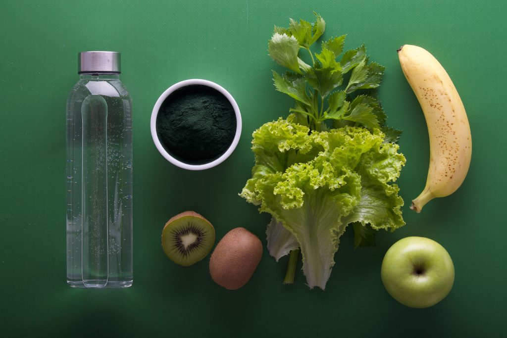 Alimentos verdes e garrafa d'água sobre uma mesa 