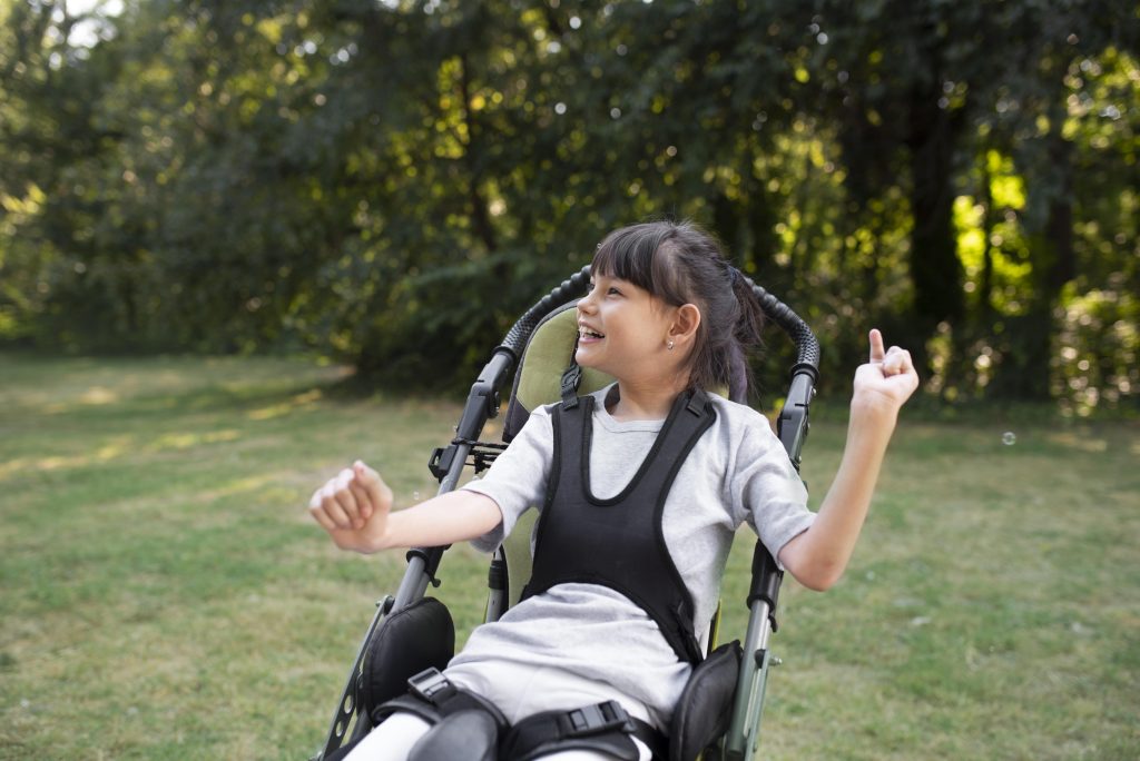 Menina com paralisia cerebral sorri sentada na sua cadeira de rodas em um parque