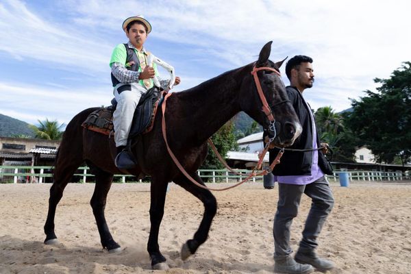 Garoto com roupa de festa junina em cima de um cavalo, que é puxado por um cuidador