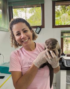 A veterinária Aline Goulart sorri para a câmera segurando uma lontra no colo
