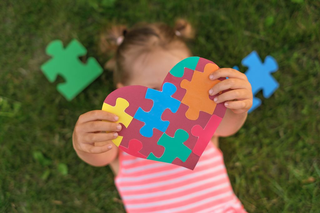 Criança segura coração feito com peças de quebra-cabeças, símbolo do autismo